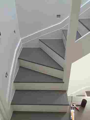 A modern, minimalist staircase with sleek white steps and a gray runner, featuring a stylish zigzag design and good lighting.
