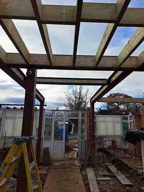 House refurbishment in Romford features partially constructed building with wooden beams overhead, an open doorway, and a ladder amidst scattered construction materials