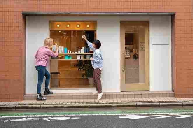 Two women arrange colorful products on a shelf outside a store renovated in Romford, preparing the display for customers. A welcoming storefront is visible.
