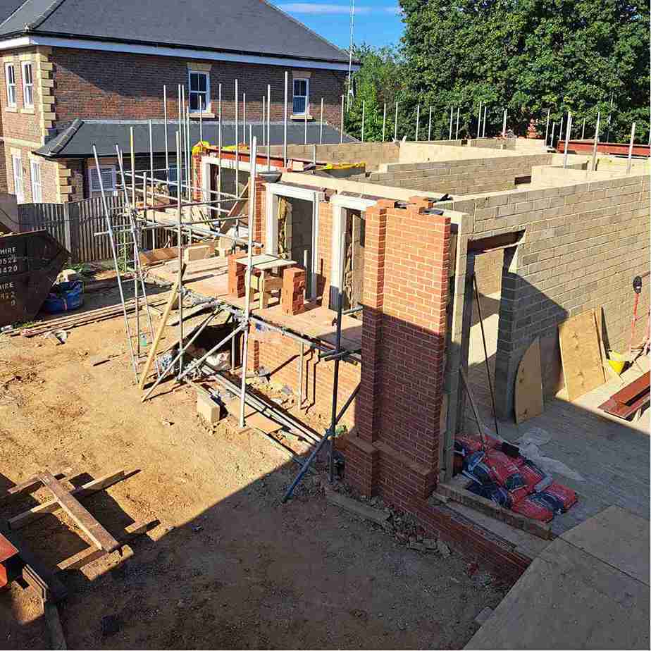 Construction site featuring brick walls and scaffolding, with tools and materials visible on the ground, alongside an unfinished building.