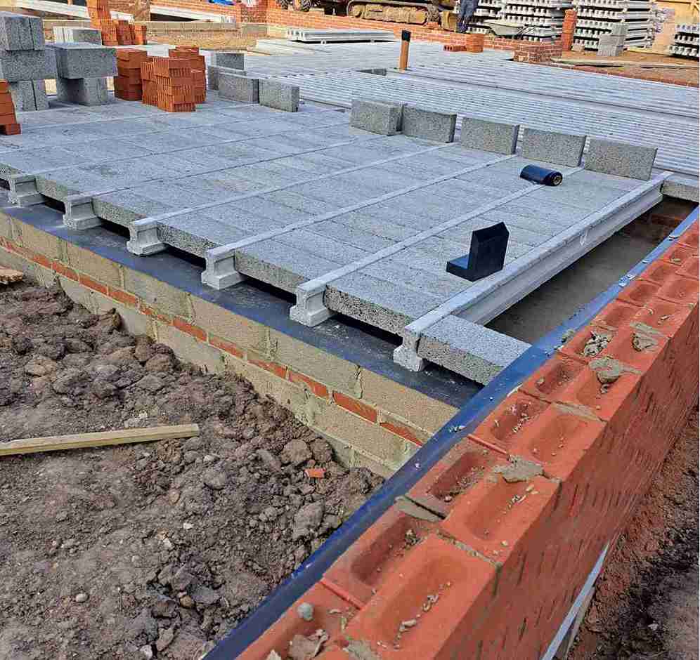 Construction site featuring grey concrete blocks laid on a foundation, surrounded by red bricks and scattered materials.