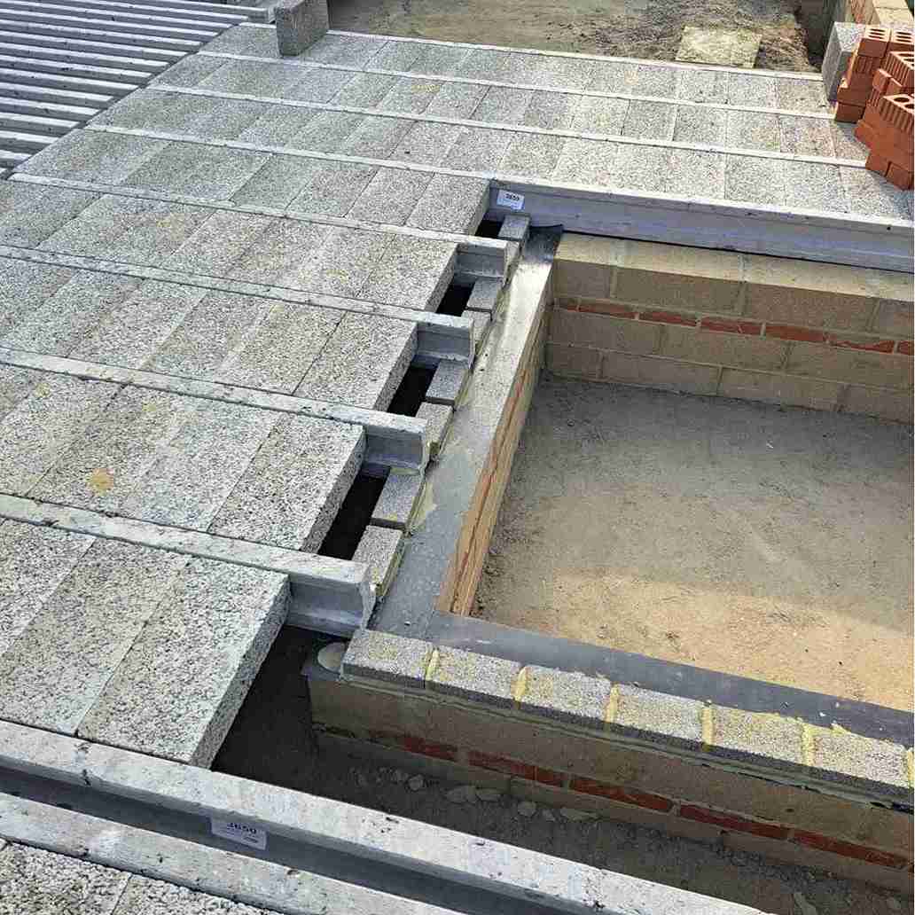 Construction site showing interlocking concrete blocks with metal supports and a framed foundation area, ready for further building work.