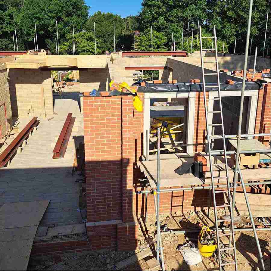 Construction site with brick walls, scaffolding, and wooden beams under a clear blue sky, showing progress on a new building.