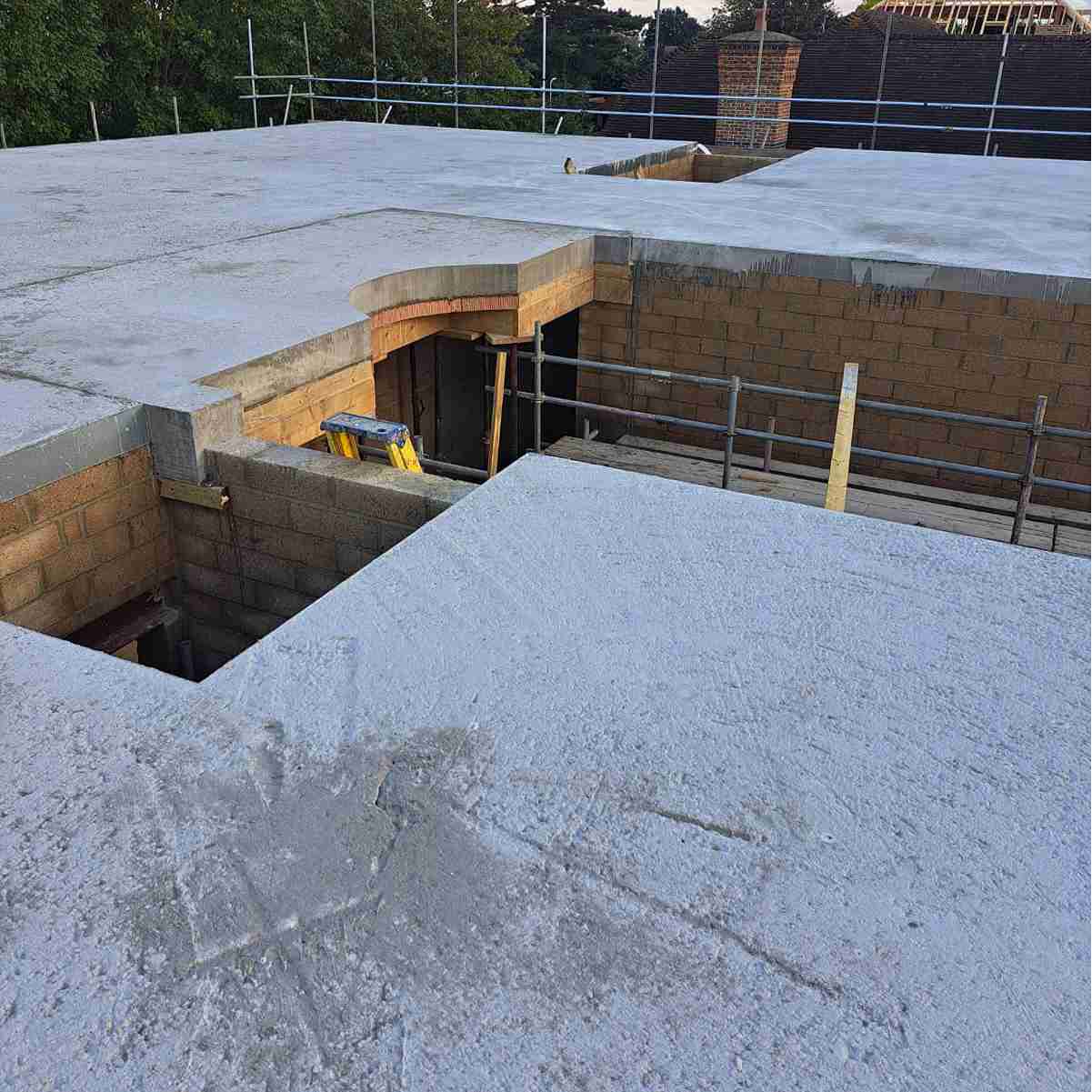 Construction site view showing concrete slabs with a curved edge, scaffolding in the background, and unfinished walls below.
