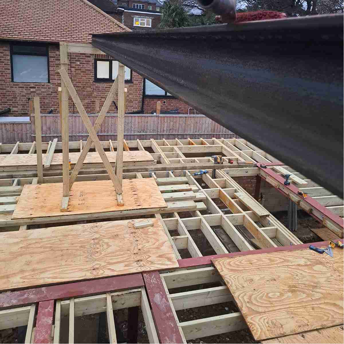 Construction site showing wooden beams and scaffolding, with a focus on a vertical support amid a framework of plywood and beams.