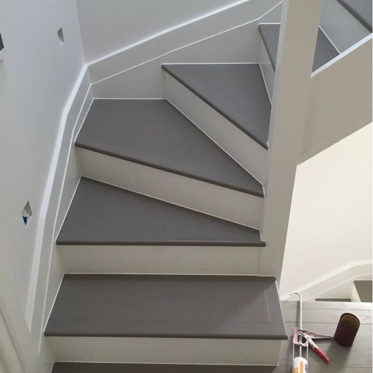 A modern, gray stairway with sleek, white walls and a partially visible railing, showcasing minimalist design elements.