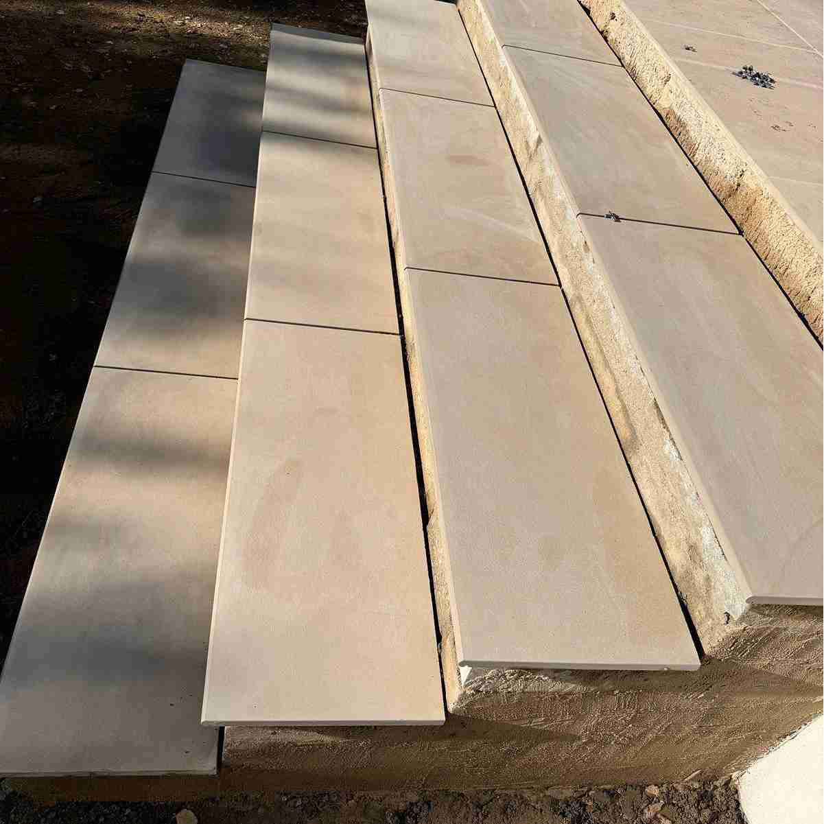 Close-up of new stone steps with large, smooth tiles laid on a sloped surface, partially completed with visible mortar.