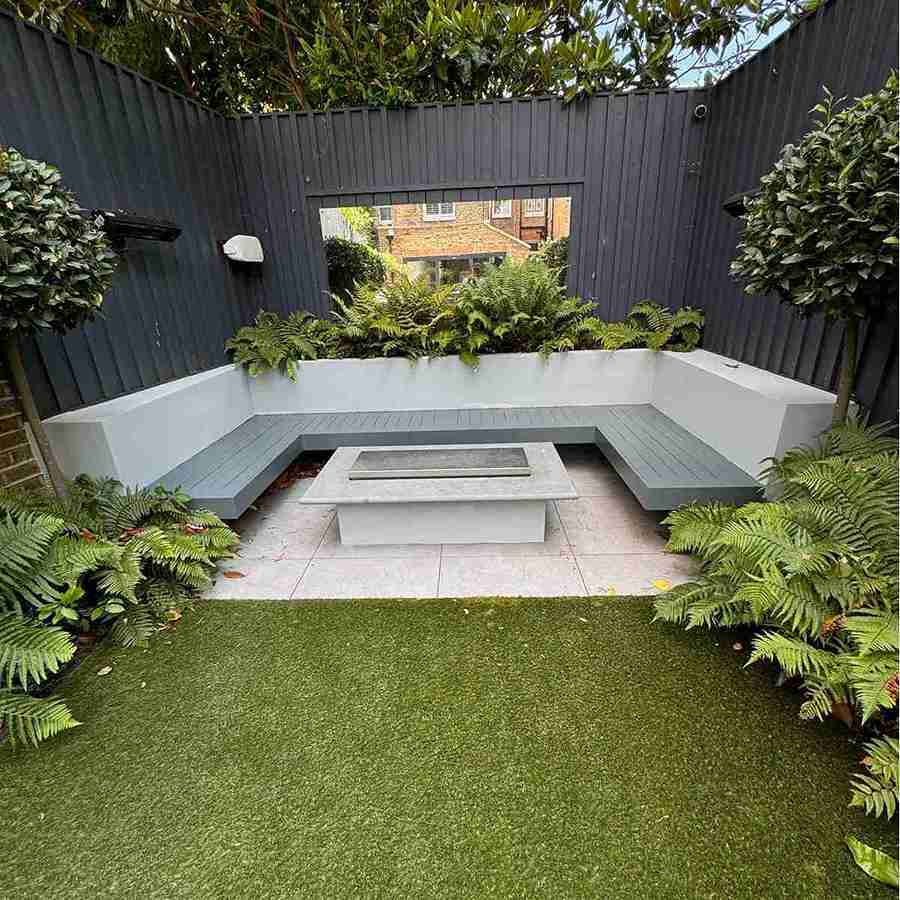 Modern outdoor garden with a stone fire pit, gray L-shaped bench, and new fencing installed in an East London home.